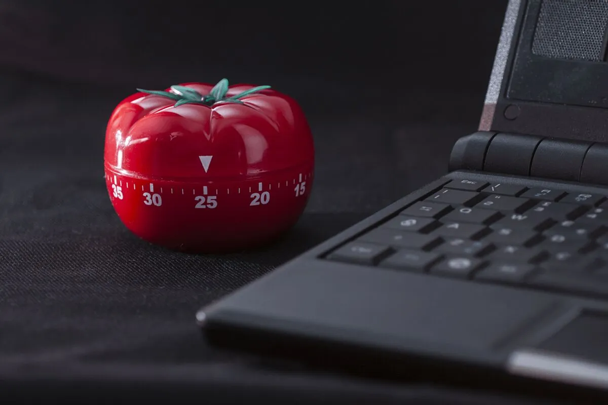 Kişinin elinde bir saat tutarak Pomodoro tekniğini kullanarak çalıştığı odaklanmış bir çalışma masası sahnesi